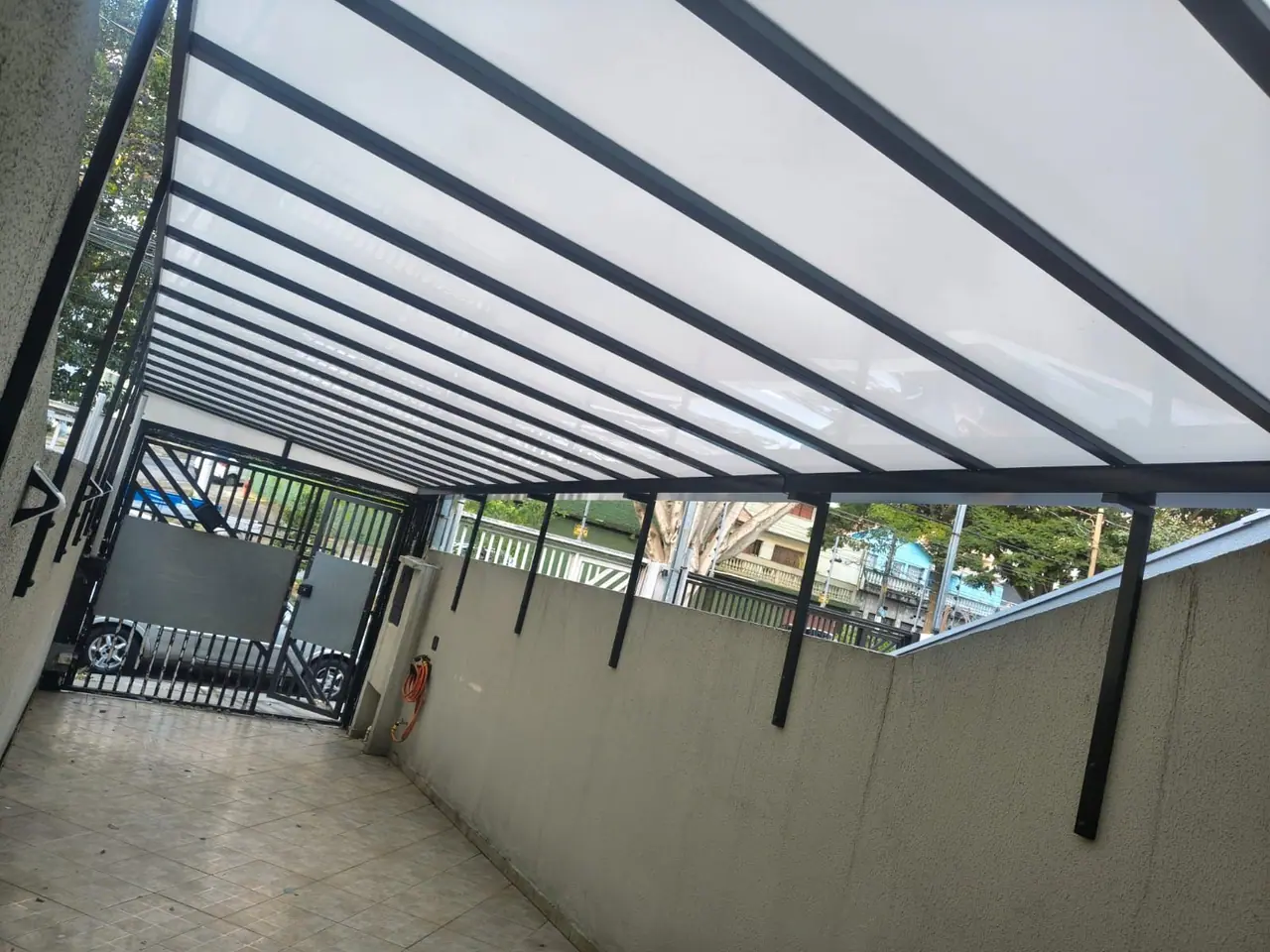 Cobertura fixa de policarbonato branco com estrutura preta na garagem em São Paulo